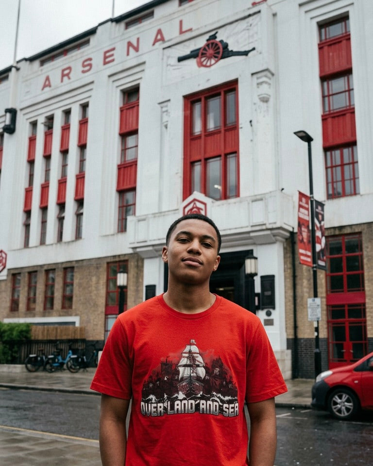 Arsenal supporter in red Over Land and Sea Champions League tee outside a North London ground.